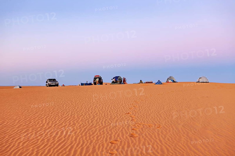 Cars and tents on a sand dune at sunrise with soft pastel colours in the sky, camping in the sand dunes of the Sahara in Algeria