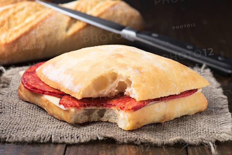 Close-up of a freshly made chorizo sandwich with sliced chorizo and mozzarella cheese, served on rustic bread. Ideal for deli menus and food blogs