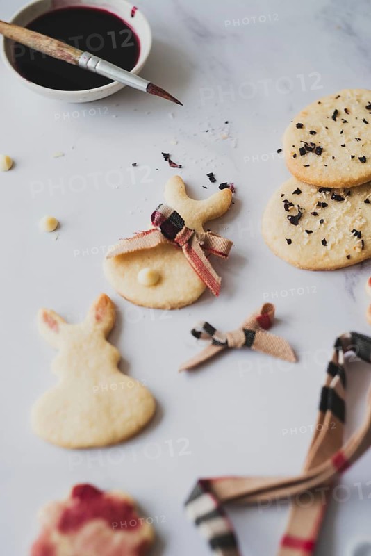 Top view of homemade Easter bunny cookies creatively painted with hibiscus tea, paired with a paintbrush and some scattered cookie crumbs on a white surface. A festive and charming springtime baking project