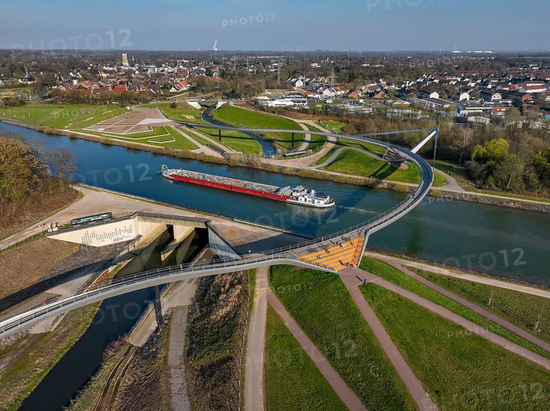 Castrop-Rauxel, North Rhine-Westphalia, Ruhr region, Germany - Sprung bridge over the Emscher, here with barge on the Rhine-Herne Canal, a footbridge and cycle bridge across the Emscher and the Rhine-Herne Canal. EMSCHERLAND adventure park, new nature and water adventure park on the restored Emscher, at the Emscher water cross with the Rhine-Herne Canal on the city limits of Recklinghausen and Castrop-Rauxel. Flood protection through area expansion. The ecological focus at the confluence of the Suderwicher Bach and Emscher rivers will also be a future garden of the IGA 2027 International Garden Exhibition. Before the restoration, the river system of the Emscher was an open, aboveground waste water channel, mixed water channel with surface water and waste water