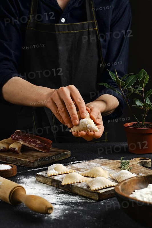 Hands skillfully shape traditional dumplings in a warm kitchen atmosphere. Flour covers the table, while ingredients like meat and herbs are prepared, reflecting a love for homemade cuisine.