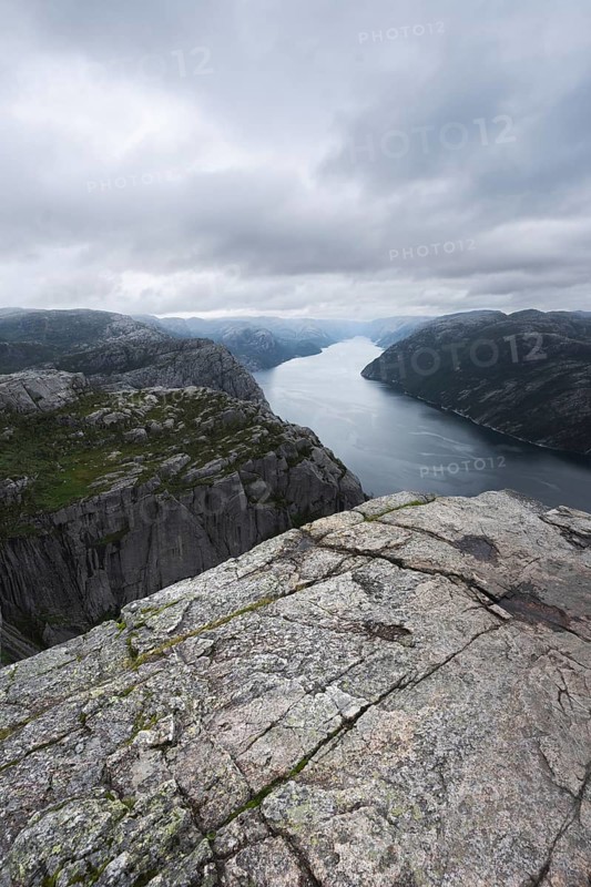 A breathtaking view of a Norwegian fjord framed by rugged cliffs under a cloudy sky, ideal for camping and trekking enthusiasts on a road trip exploring nature's wonders