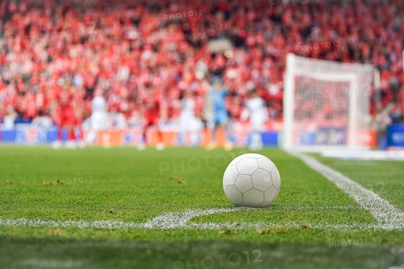 White ball at the corner of soccer pitch with players and fans in background in Lodz, Poland
