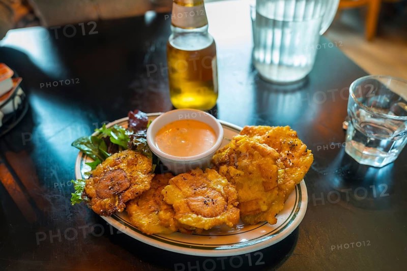 Fried plantain tostones served with a creamy dipping sauce and a side salad, creating a vibrant, appetizing meal on a dark table in a casual restaurant setting