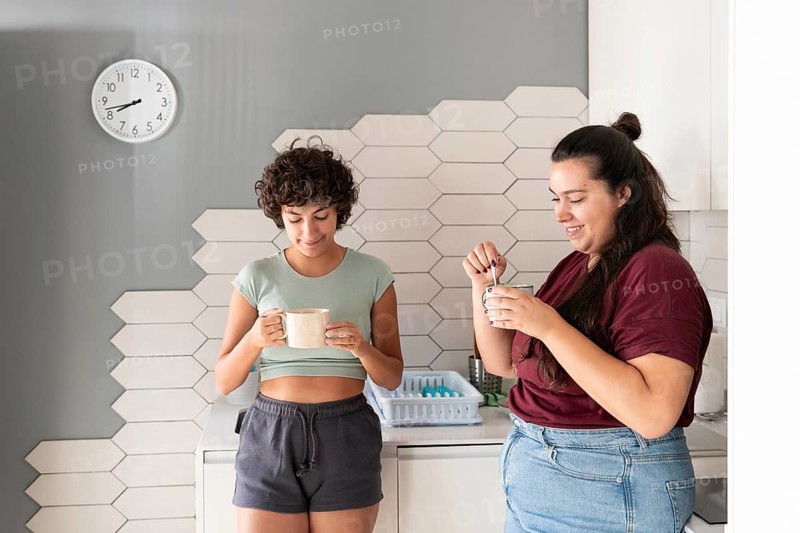 A loving lesbian couple enjoys a morning coffee together in their modern kitchen. They share smiles and warmth, creating a cozy and intimate atmosphere