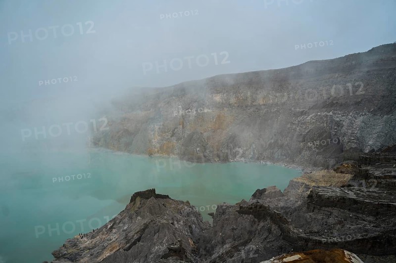 A turquoise acidic lake within the crater of Ijen volcano in Indonesia, surrounded by rocky terrain and partially veiled by volcanic mist from sulfur gas emissions