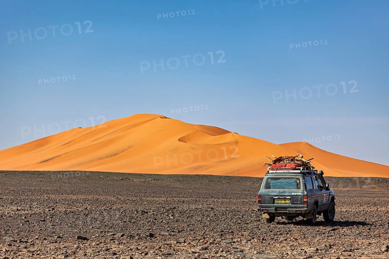 An off-road vehicle drives through an expansive desert with an impressive dune, By off-road vehicle through the Sahara desert in Algeria