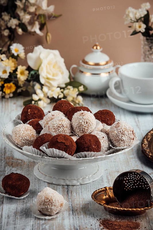 Decorative arrangement of chocolates on a porcelain dish, flowers and crockery in the background