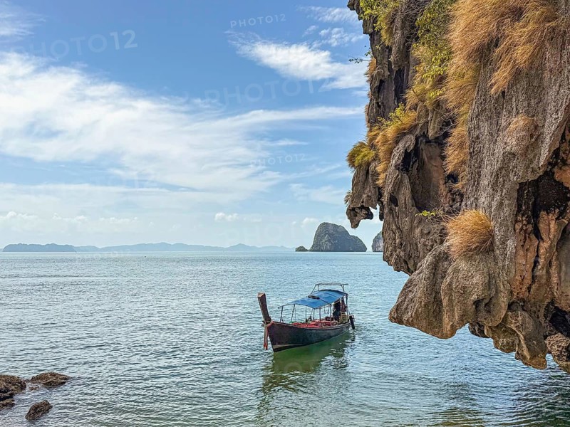 Breathtaking coastal views of Phuket, Thailand, featuring a traditional longtail boat gliding through serene turquoise waters against a backdrop of rocky cliffs and lush greenery