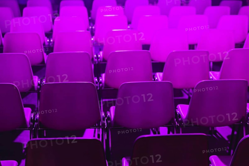Empty rows of chairs with a vibrant purple light illuminating them at a conference of AI in Amsterdam. Perfect for concepts of events, conferences, or modern design with an artistic touch