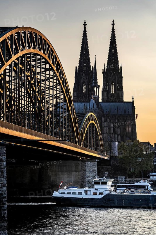 Silhouettes of the cathedral in late sunlight, freighter on the Rhine, view of Cologne Cathedral and the Hohenzollern railway bridge over the Rhine near Cologne, North Rhine-Westphalia, Germany