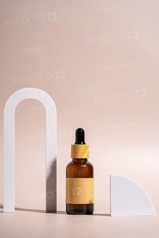 A minimalist setup featuring a brown glass dropper bottle with wooden cap, placed on a beige background accented by white geometric shapes, capturing elegance