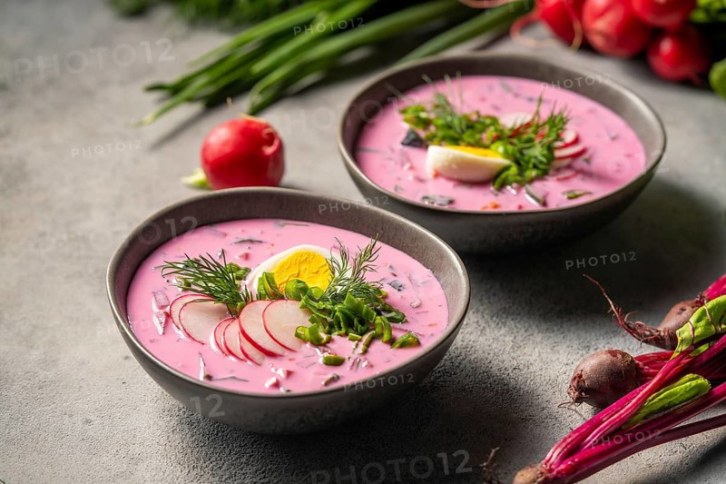 Fresh cold beetroot soup in bowls garnished with sliced radish, boiled egg, and fresh dill, set against a rustic background, capturing the essence of healthy summer dining