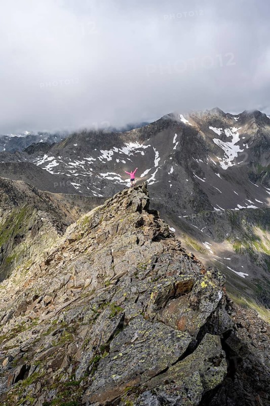 Mountaineer stretching her arms in the air, on a steep rocky ridge, on the summit of the Lasörling, Lasörling Group, Hohe Tauern National Park, East Tyrol, Tyrol, Austria