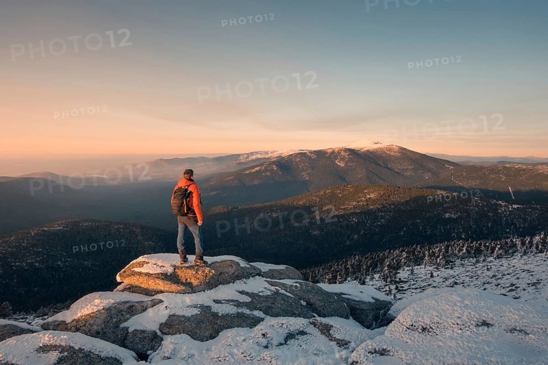 A hiker in a red jacket stands on a snowy peak in Siete Picos, Guadarrama Mountains, gazing at the stunning mountain view during sunrise. Captures the essence of adventure and serenity