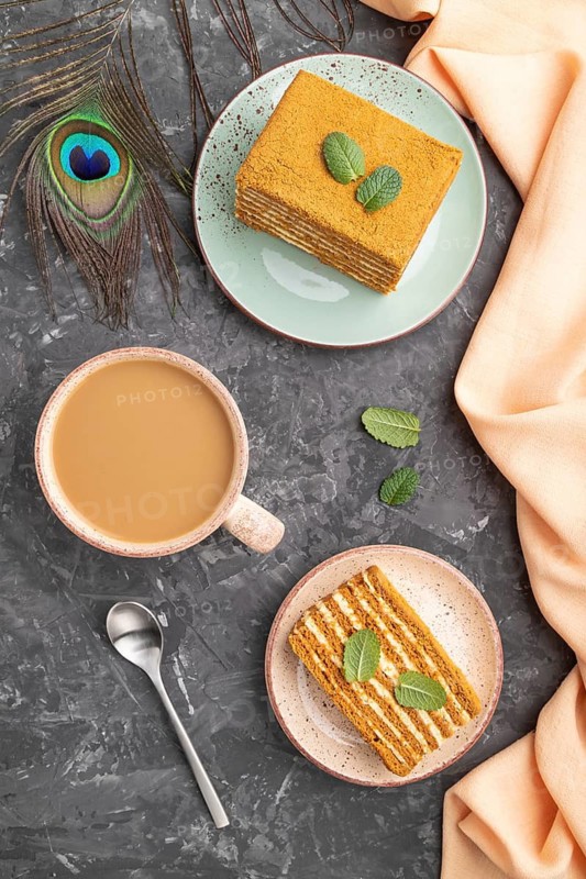 Homemade honey cake with milk cream and mint with cup of coffee on a black concrete background and orange textile. top view, flat lay, close up