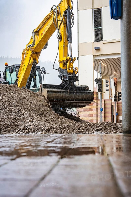 Large excavator moving earth on a construction site in the rain, building in the background, Hermann Hesse railway construction site, Calw, Black Forest, Germany