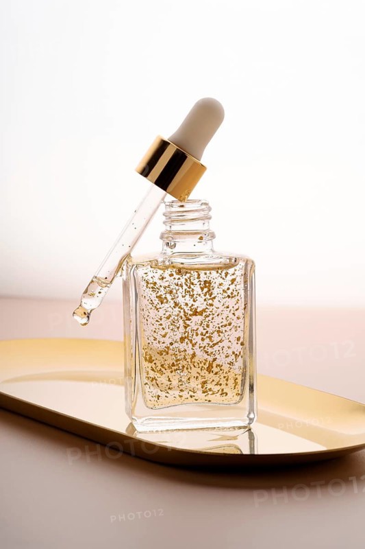 Elegant glass dropper bottle filled with anti-aging face serum, featuring suspended golden particles, highlighted against a soft neutral background