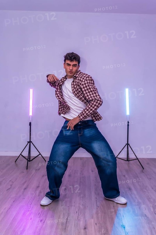 Young man dancing in a studio illuminated by led lights, showcasing energetic moves and expressing passion through dance