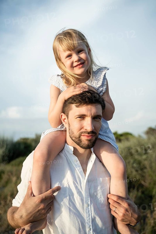A loving father carries his smiling daughter on his shoulders during a warm summer day in Italy. They enjoy a joyful and carefree moment together in nature, creating cherished memories
