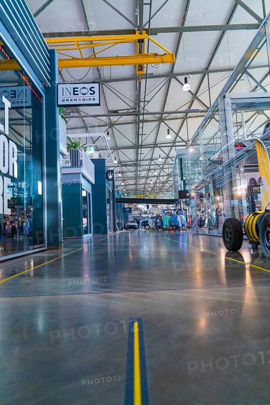 Spacious, modern room in industrial hall with steel structures and glass panes, warm yellow tones, Motorworld Böblingen, Germany