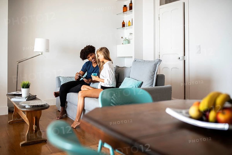 A cheerful couple sits on a modern sofa in a cozy, stylish living room. They enjoy coffee and laughter, surrounded by a warm atmosphere and contemporary décor