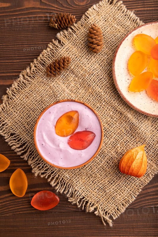 Purple Yogurt, with jelly candy on brown wooden background and linen textile, top view, flat lay, close up, minimalism