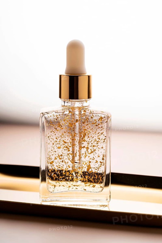 High-end anti-aging face serum bottle enriched with shimmering gold particles against a soft blurred background, highlighting luxury skincare