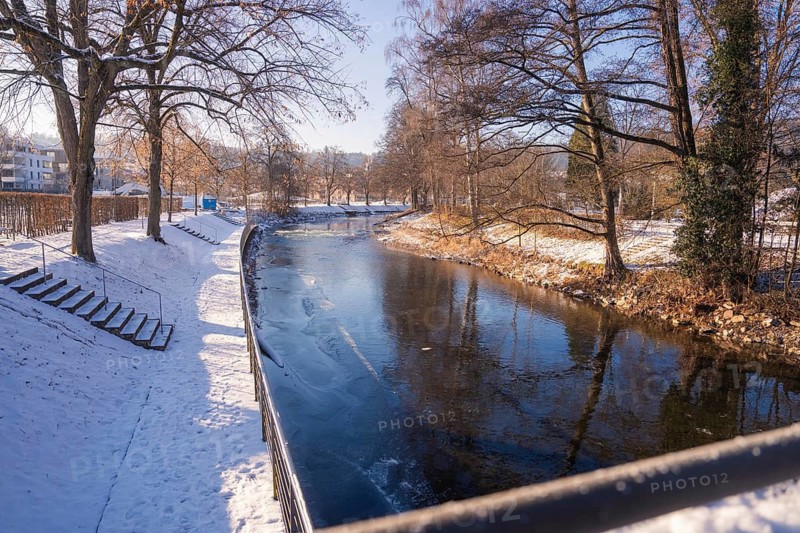 Snowy river landscape with bare trees and reflecting water under a clear sky, Nagold, Calw district, Germany