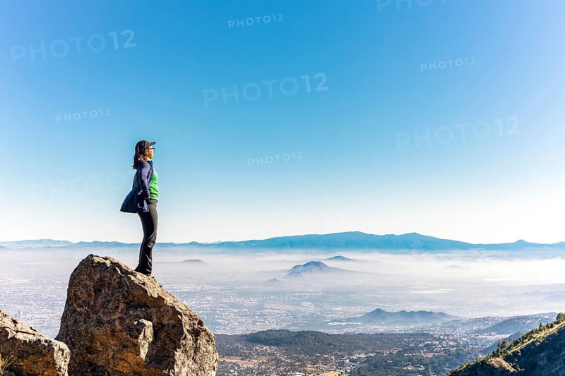 A person stands on a rock, overlooking a breathtaking mountain landscape under a clear blue sky The scene evokes a sense of freedom, exploration, and adventure