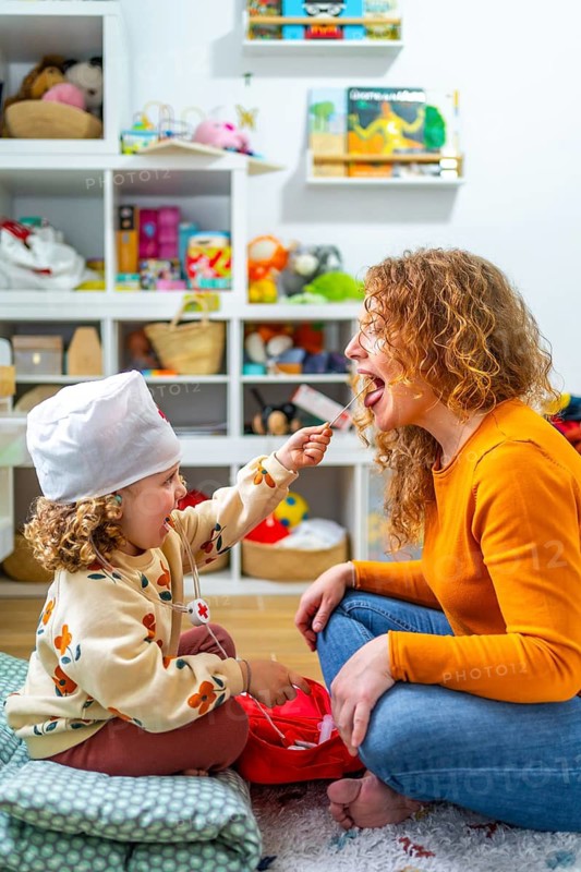 Vertical photo of a cute caucasian girl examining the tongue of her mother playing nurses