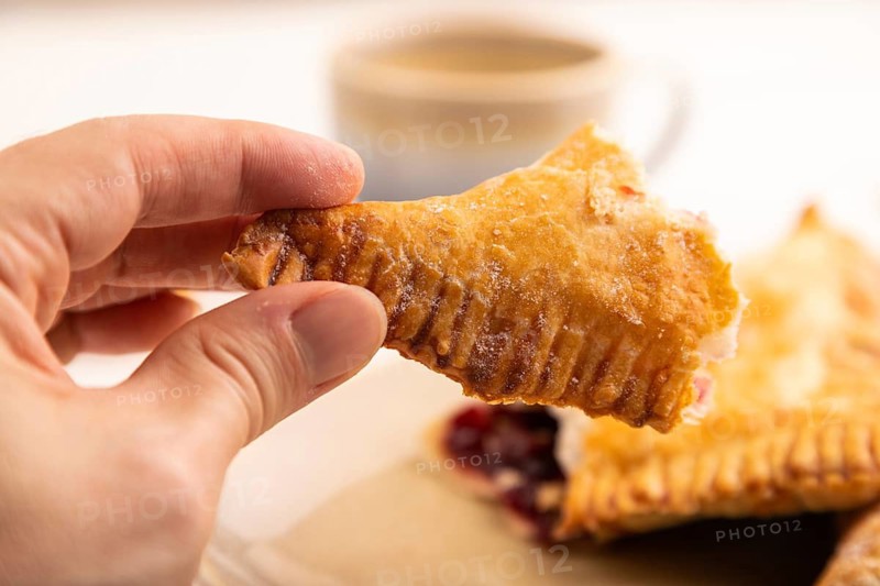 Triangles Pie, Puff Pastry, Samsa with cherry jam with hand on white wooden background, cup of coffee, side view, close up, selective focus