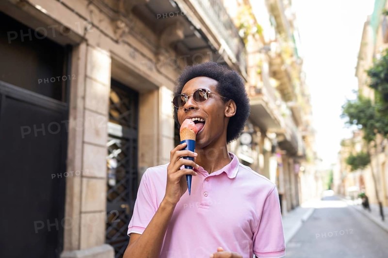 A happy non-binary individual enjoys a refreshing ice cream cone on a sunny day. They smile joyfully, embodying freedom and warmth in an urban setting, wearing casual attire
