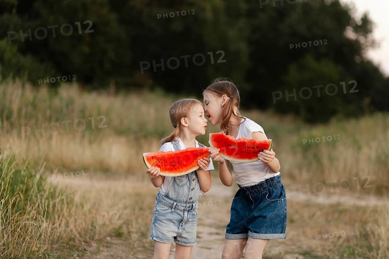 Two children happily share slices of juicy watermelon on a sunny summer day, surrounded by lush greenery, embodying the carefree joy and freshness of summertime outdoors