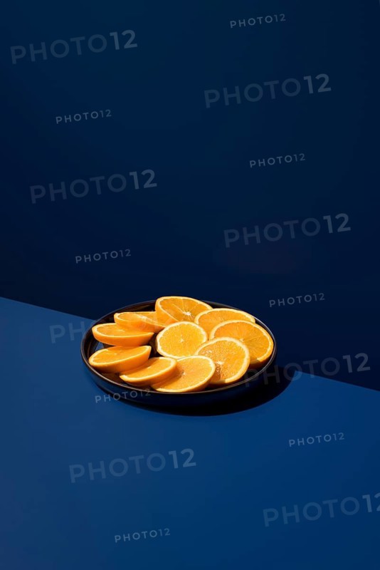 A plate of vibrant orange slices arranged neatly on a dark blue surface. The contrast highlights the freshness of the fruit, creating a visually appealing image