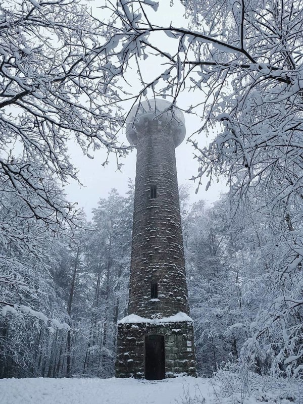 An old stone tower is surrounded by snow-covered trees in a wintery forest, Lucas Cranach Tower in Kronach, Frankenwald nature park Park