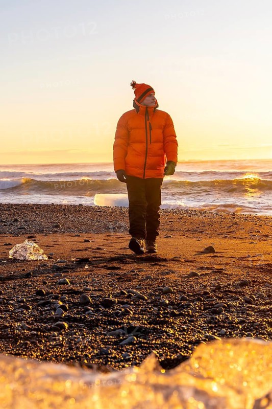 A tourist in an orange jacket walking at sunrise on Diamond Beach Iceland in winter