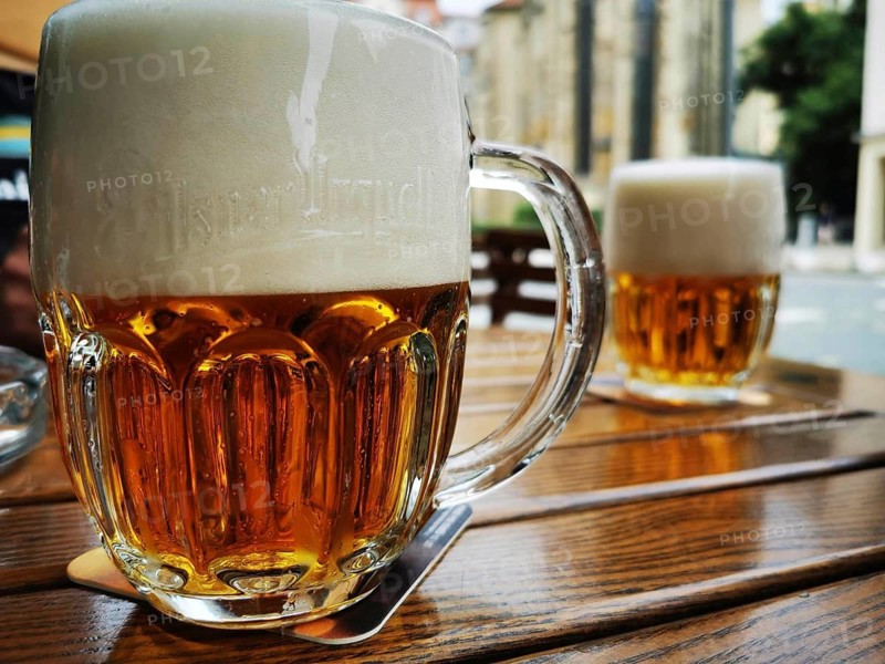 Two gold-colored glasses of beer with Pilsner Urquell inscription with foam crown on a wooden outdoor table, Pilsen, Czech Republic