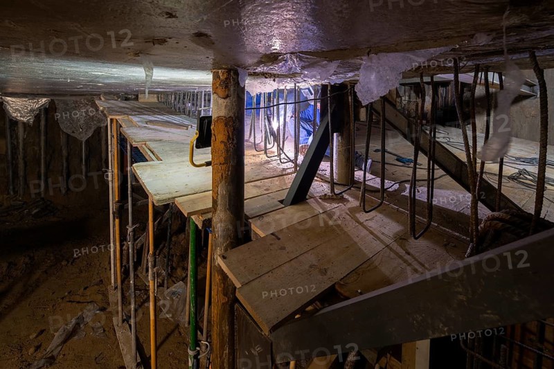 A detailed view of an underground construction site reveals complex scaffolding and steel reinforcement structures. The image captures the essence of a work in progress setting
