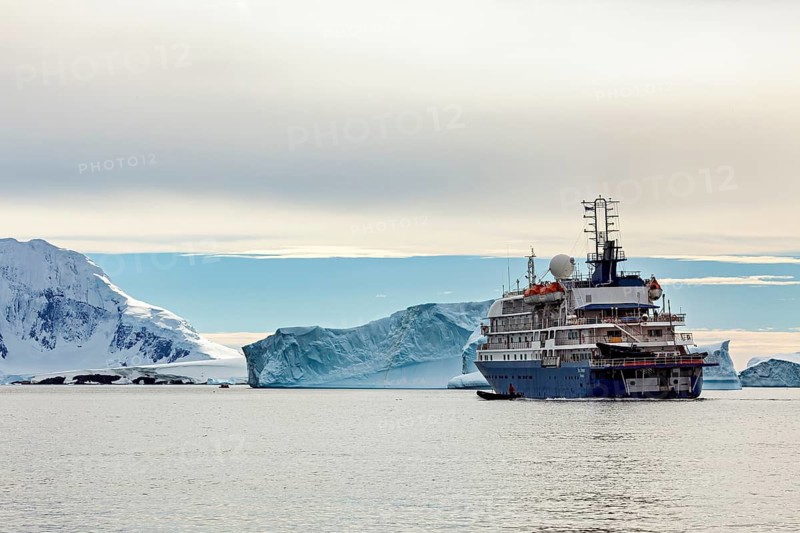 A ship sails through a tranquil Arctic landscape, past majestic icebergs under a cloudy sky, cruise ship among icebergs in Antarctica