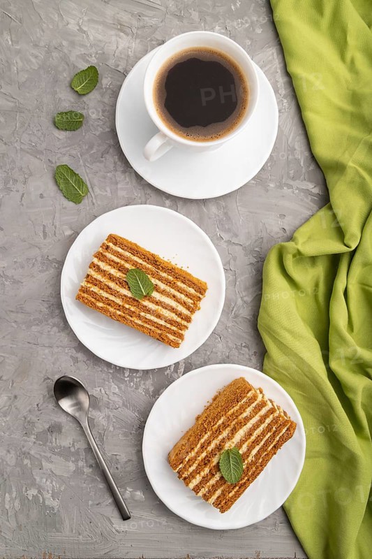 Homemade honey cake with milk cream and mint with cup of coffee on a gray concrete background and green textile. top view, flat lay, close up