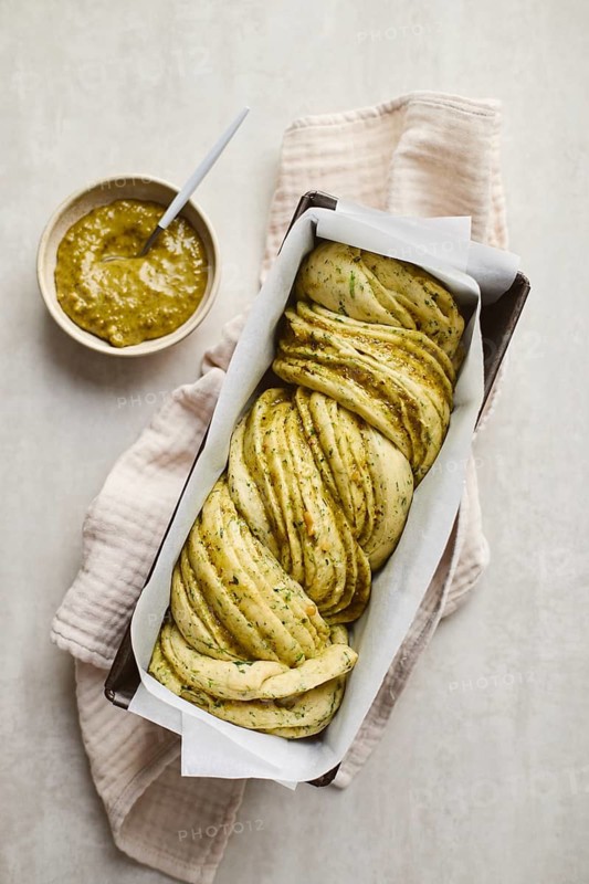 Ready to bake, homemade savoury babka plaited bread loaf flavoured with cheese and pesto, in the making tin. Top view