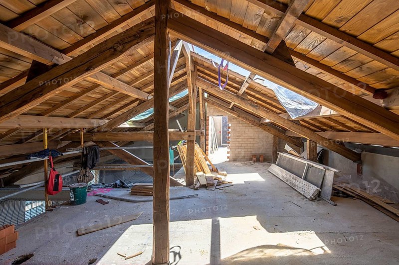 Sunlit attic with wooden beams and scattered construction materials showcases a renovation in progress, highlighting architectural transformation and potential