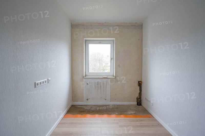 Empty room is being renovated, walls are partially wallpapered, laminate on the floor, heating pipes in the wall