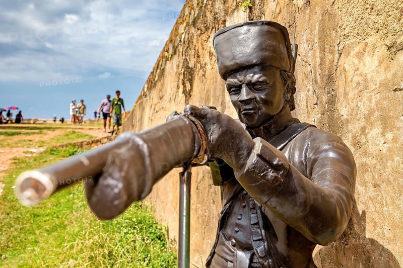 Bronze statue of a soldier pointing a rifle at a target, next to a wall, statue in the historic fortress of Galle in Sri Lanka
