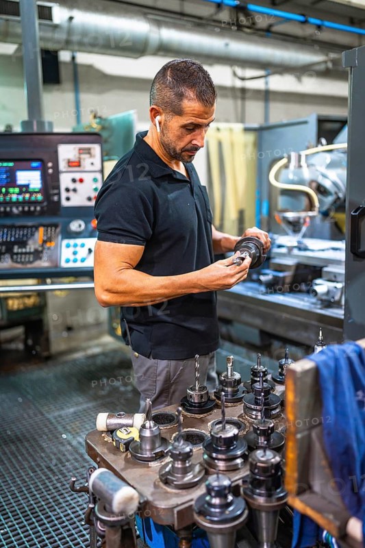 Vertical photo of a concentrated male caucasian technician working with milling machine in a cnc factory