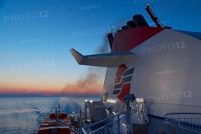 A ship leaves traces of smoke over the calm sea at dusk, New ferry port in southern Patras, Ferries, Patras, Peloponnese, Greece