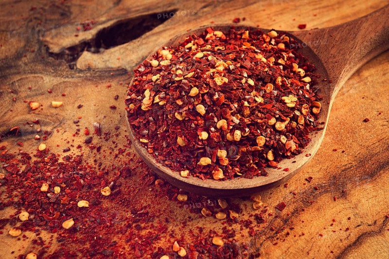 Red pepper flakes, in a wooden spoon, on a wooden table, rustic style, no people