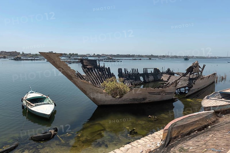 An abandoned burned out hull of a fishing boat with green plants growing inside it on the banks of the River Nile at Rosetta, the Nile Delta, Egypt