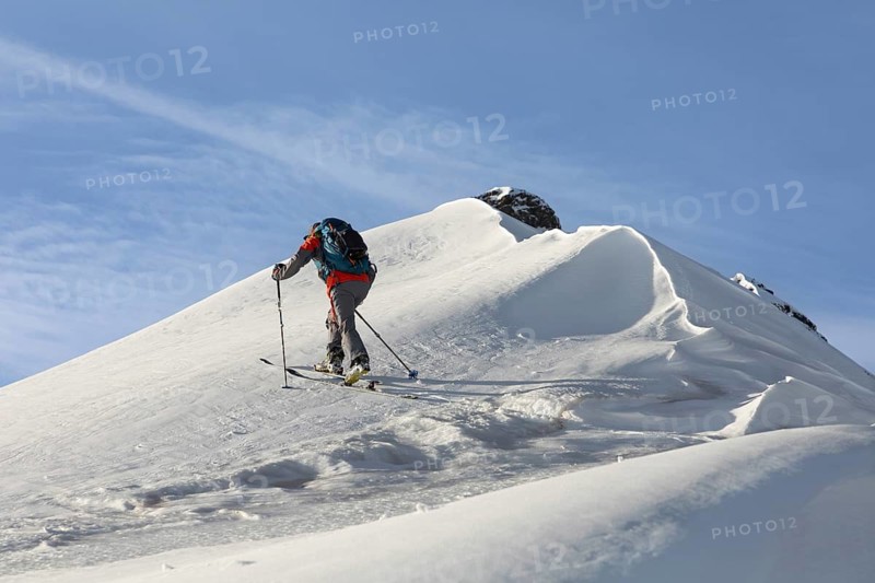 A skier tackles a snowy mountain slope with ski poles and backpack, capturing the essence of ski touring and adventure in a serene winter landscape